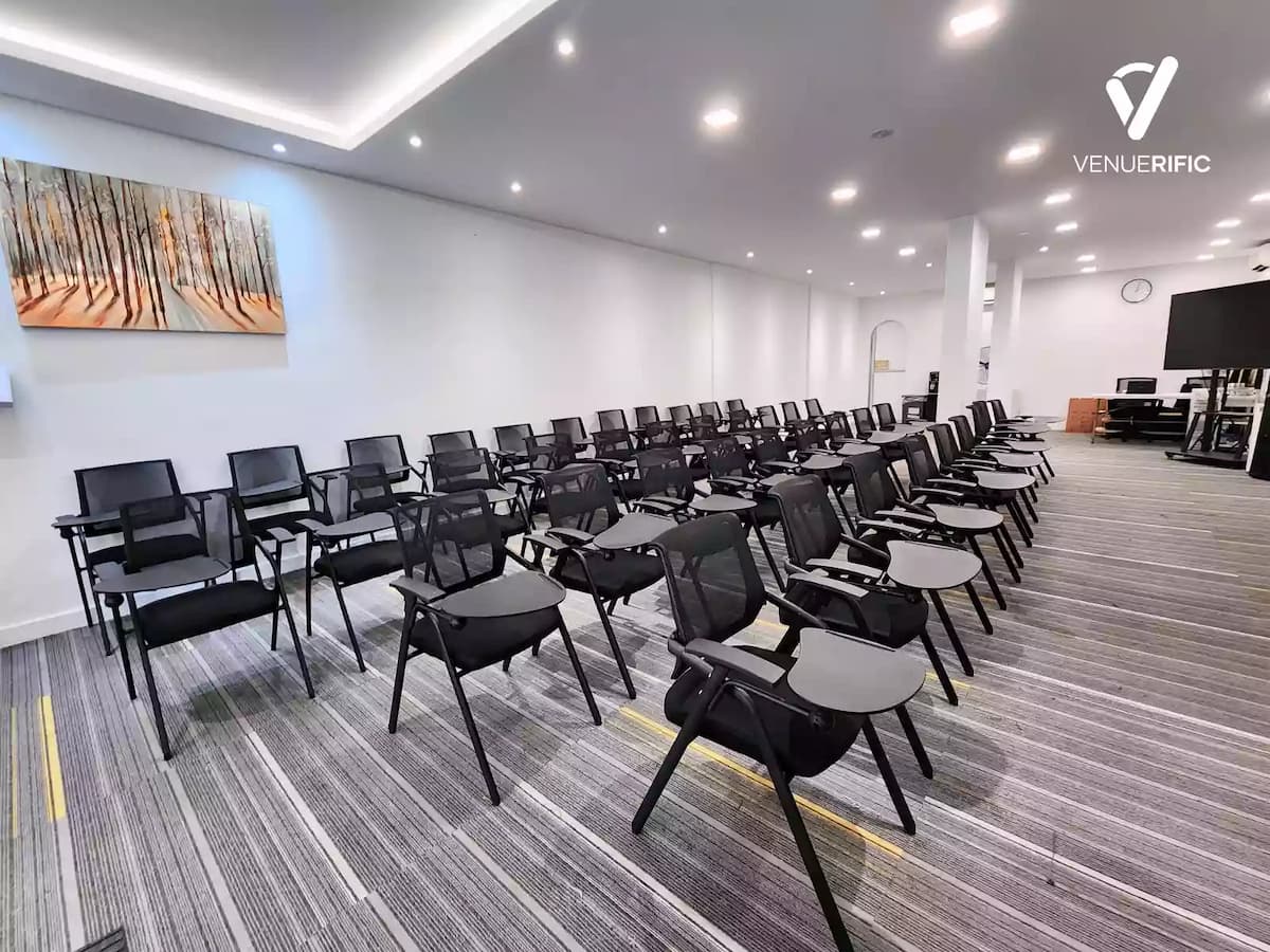 Modern training room with rows of black mesh chairs facing a large whiteboard and two flat-screen monitors.