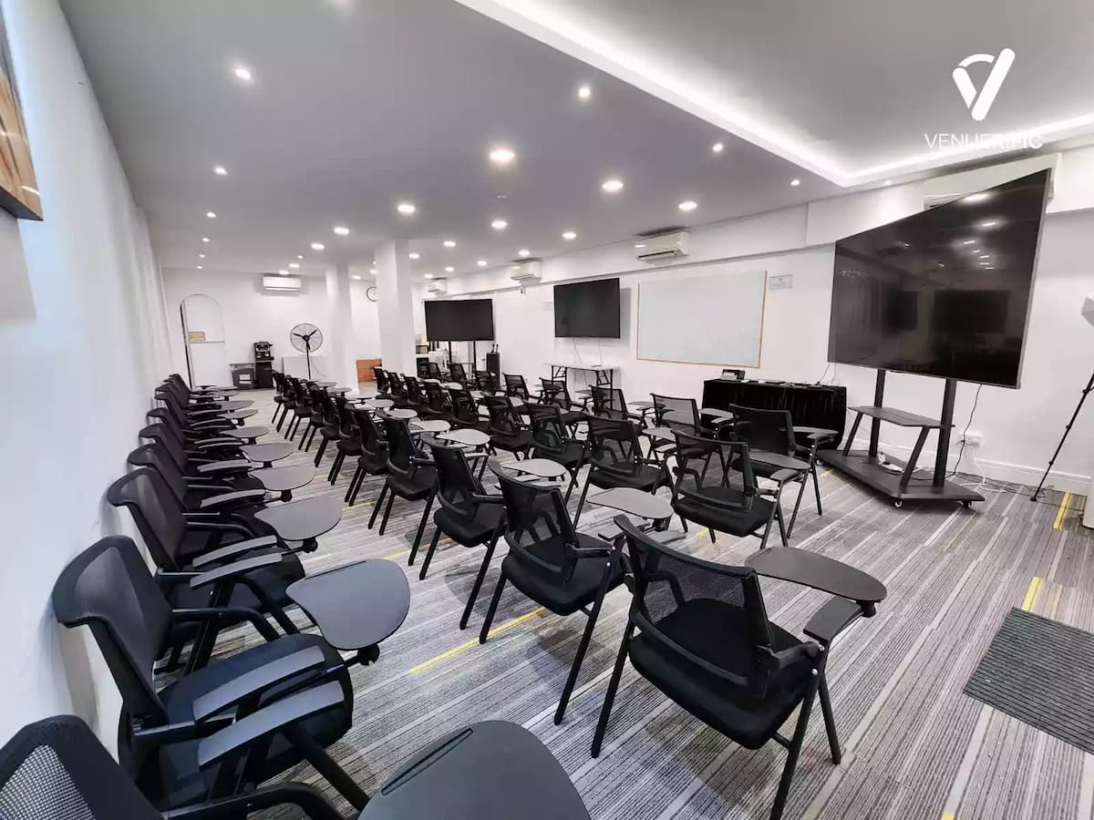 Modern training room with rows of black mesh chairs facing a large whiteboard and multiple flat-screen monitors.