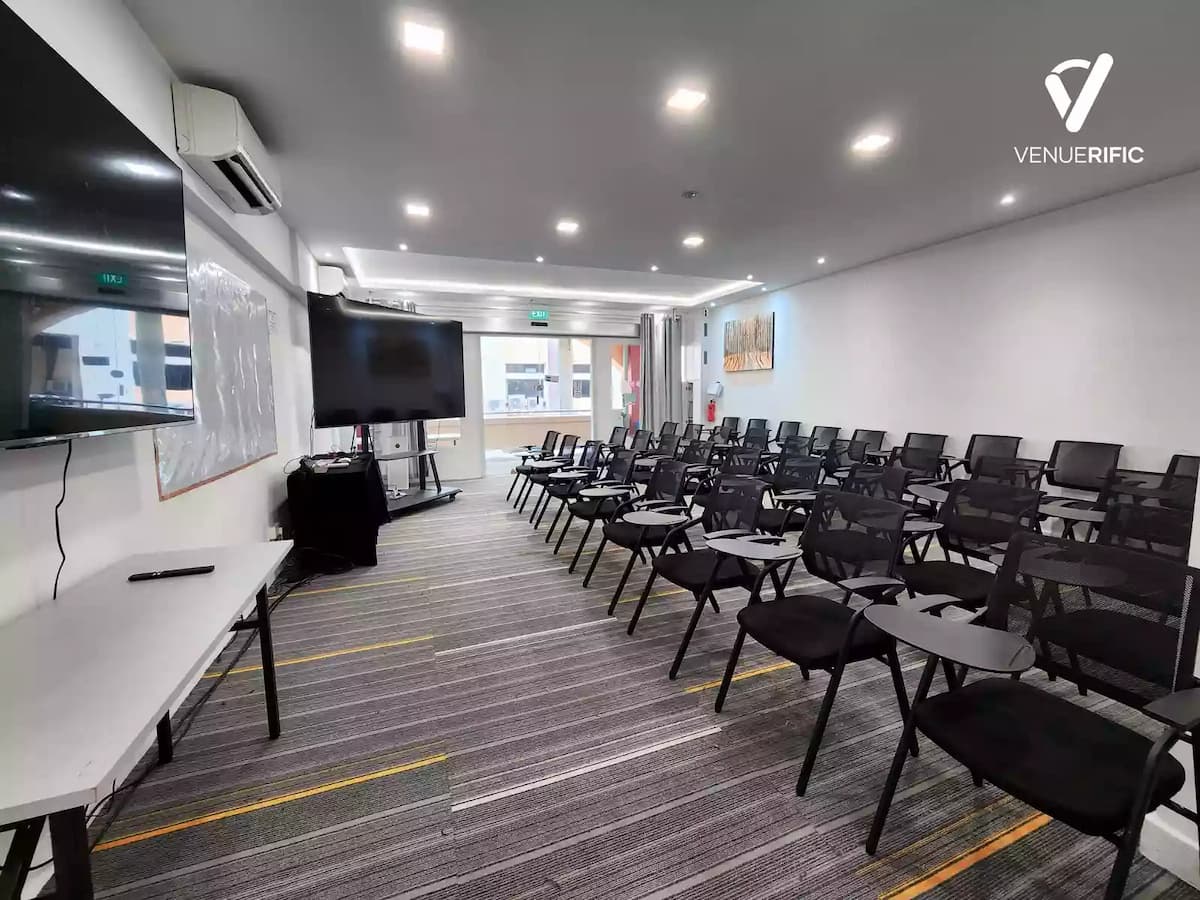 Modern training room with rows of black chairs facing a whiteboard and large monitors.