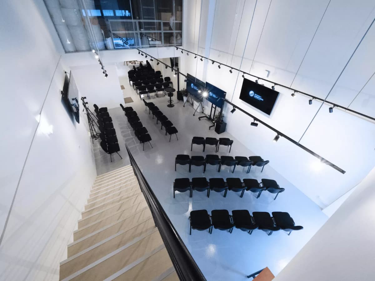 Overhead view of a modern event space with rows of black chairs, large screens, and a staircase leading down.