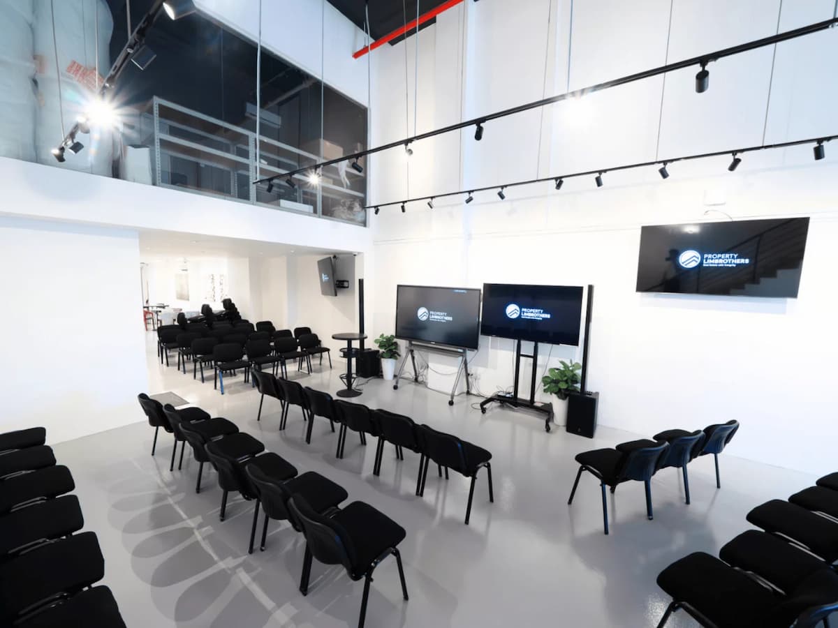 Spacious modern event hall with rows of black chairs, multiple display screens, and a mezzanine level above.