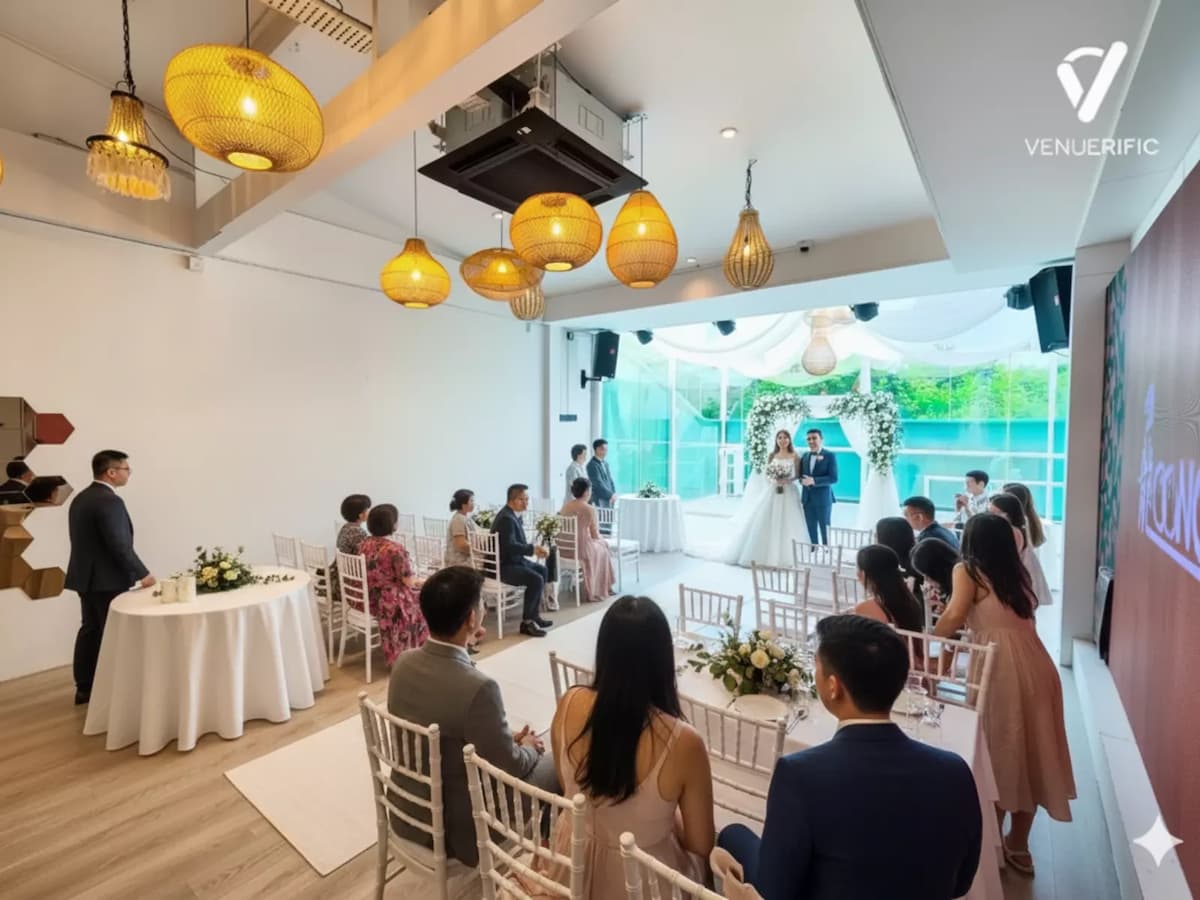 Bright indoor wedding ceremony with seated guests, warm pendant lights, and a floral backdrop by floor-to-ceiling windows.