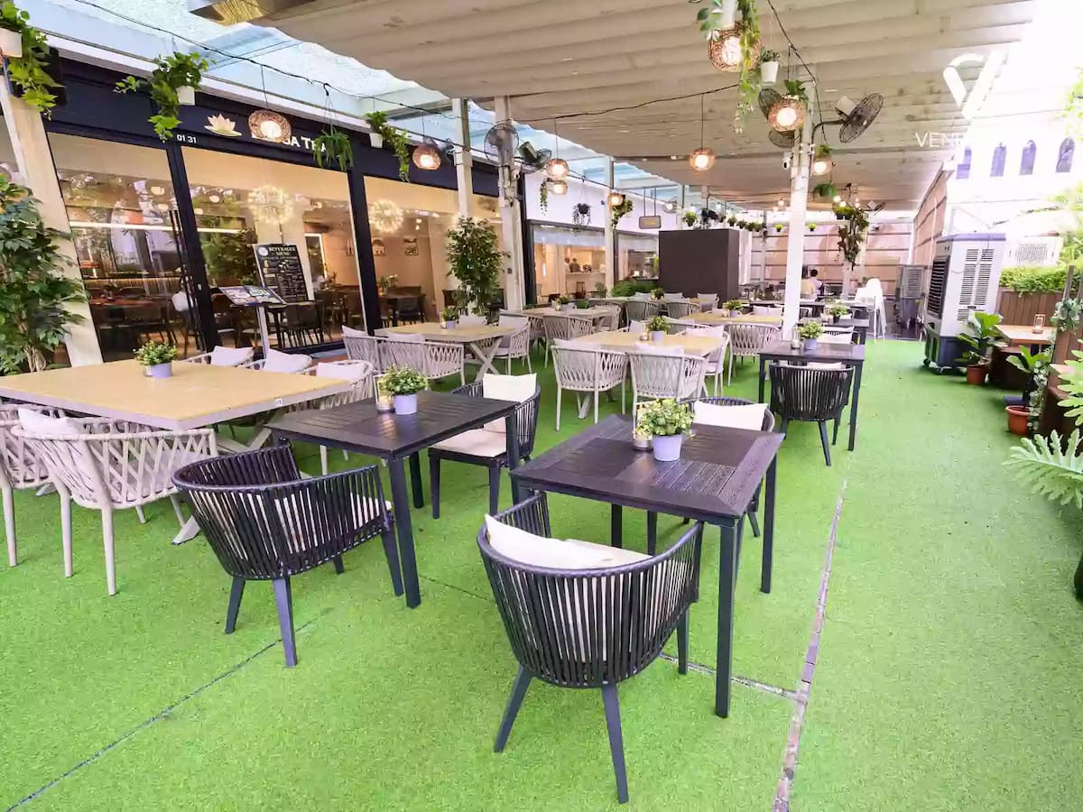 Covered outdoor event space with greenery, café tables, and ambient lighting.