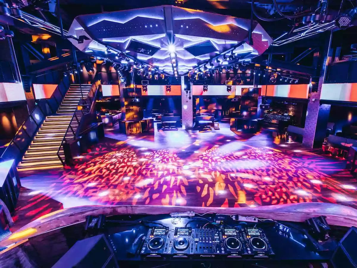High-energy nightclub interior with a DJ booth, dynamic lighting, illuminated dance floor, and multi-level seating.