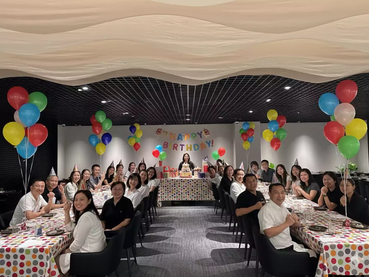 Birthday party setup with long tables, balloons, and guests celebrating indoors.