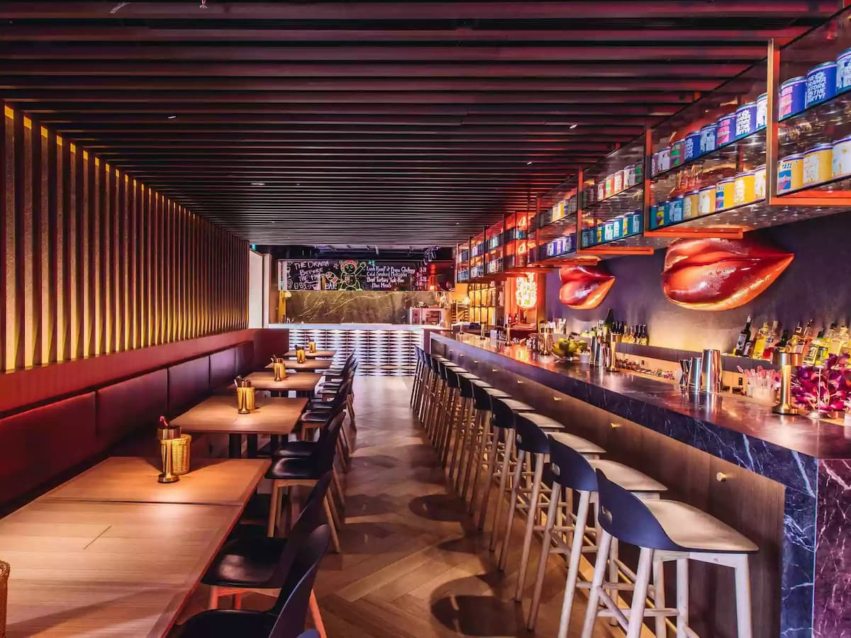 Warm, modern bar interior with long counter seating, wood accents, ambient lighting, and decorative wall displays.