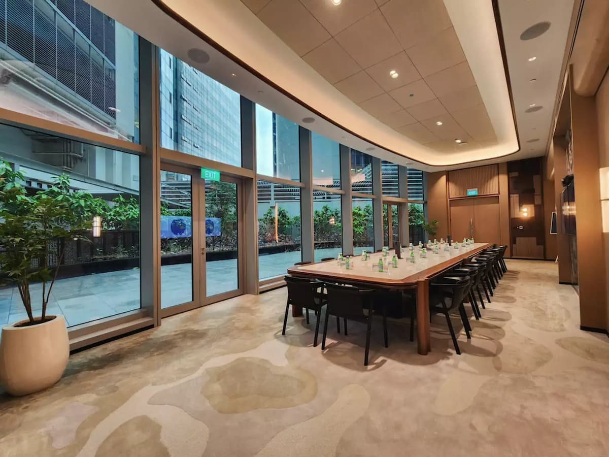 Elegant boardroom with long wooden table, black chairs, and floor-to-ceiling windows overlooking a garden terrace.