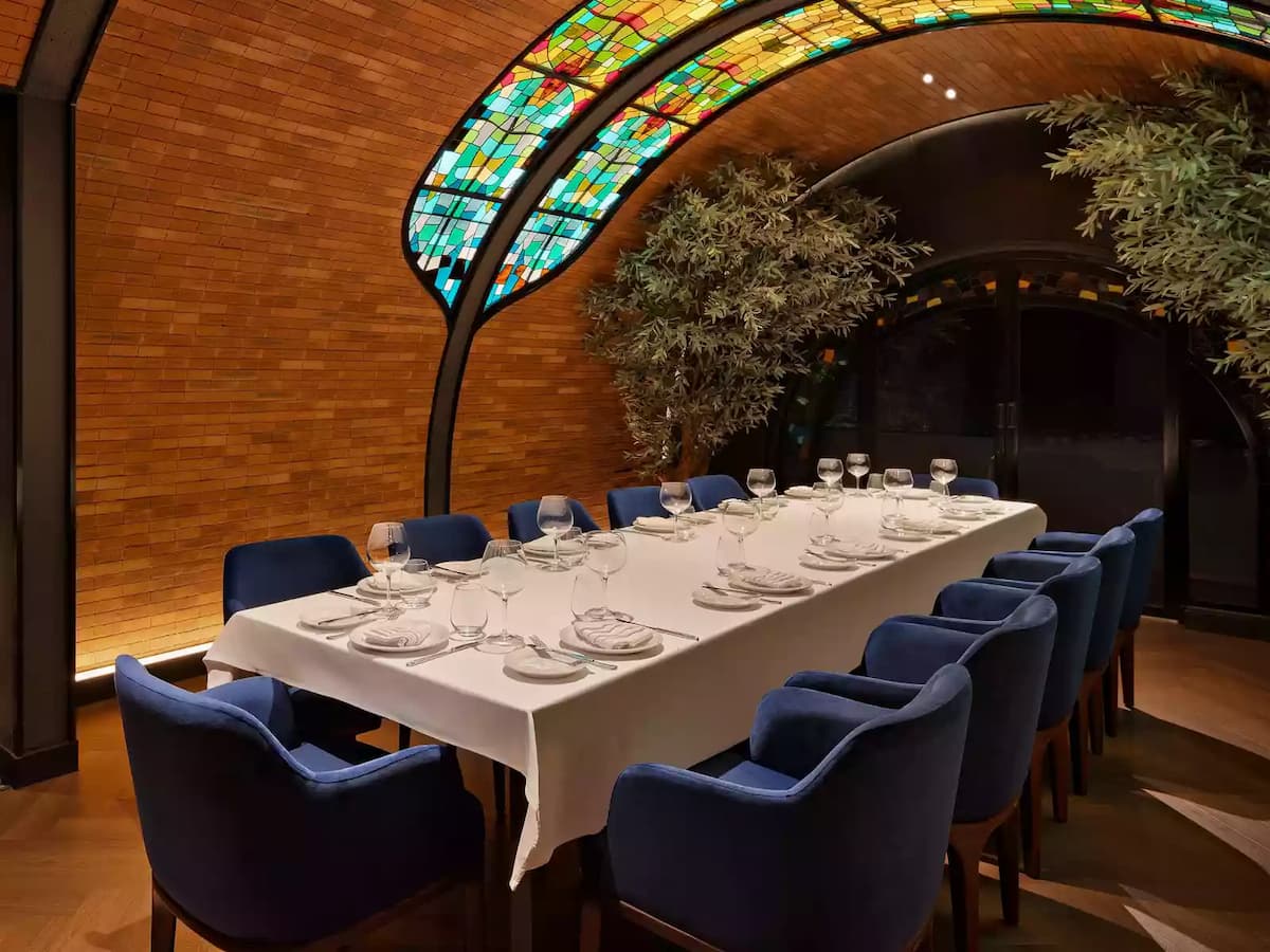 Private dining room with long set table, blue upholstered chairs, and stained glass arched ceiling.