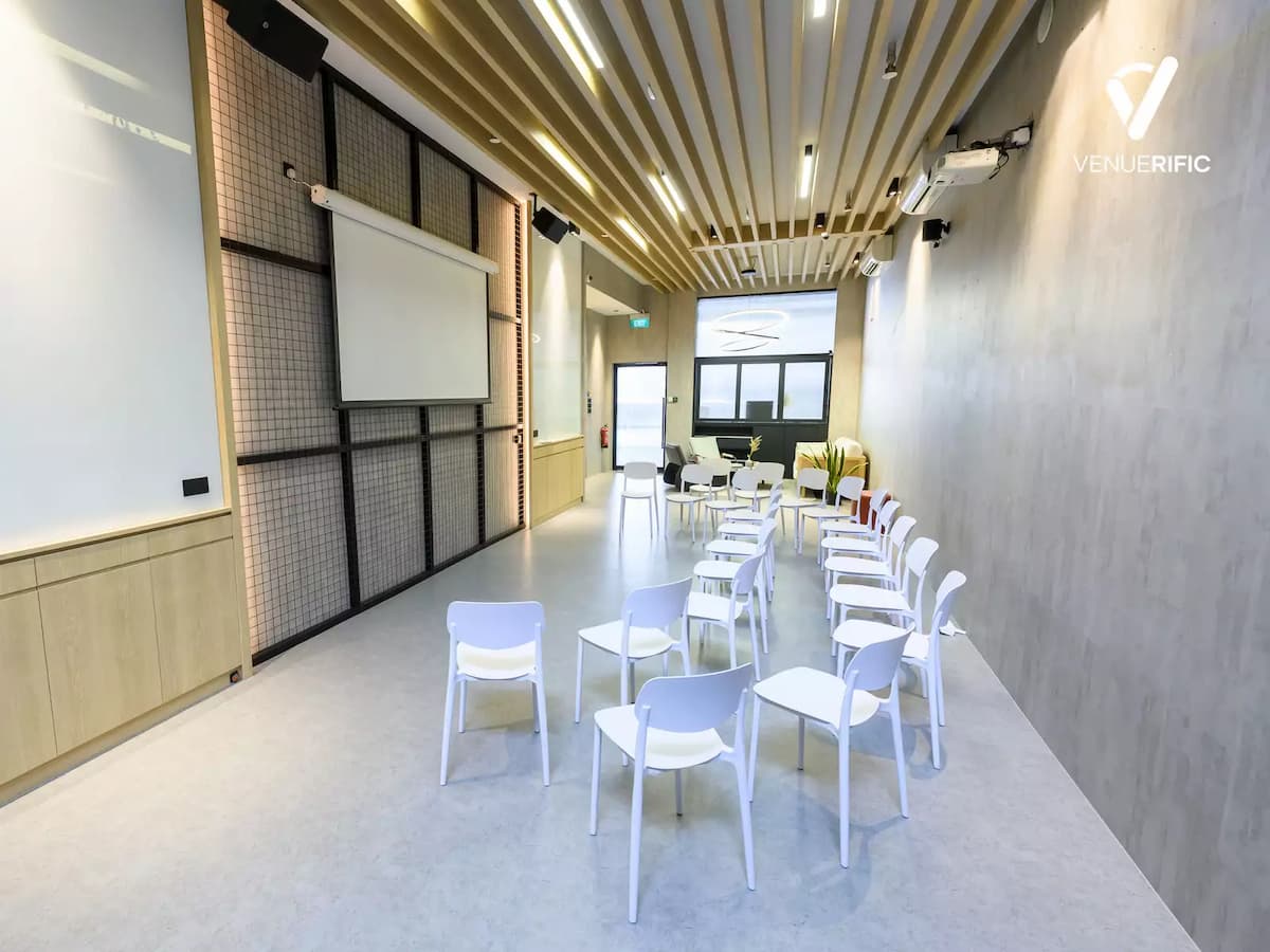 Bright presentation space with white chairs, projector screen, wood slat ceiling, and a clean, modern layout.