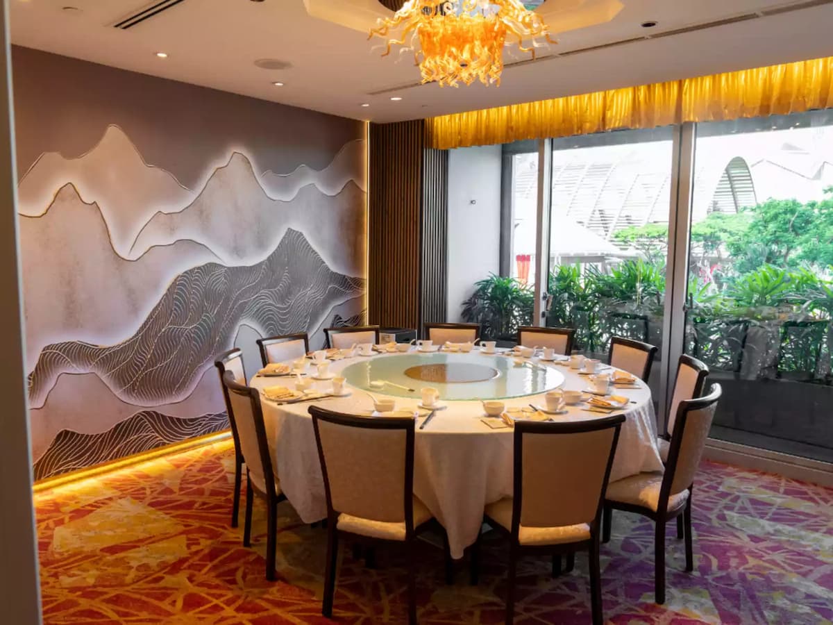 Private dining room with round table, elegant place settings, statement chandelier, and window views of lush greenery.