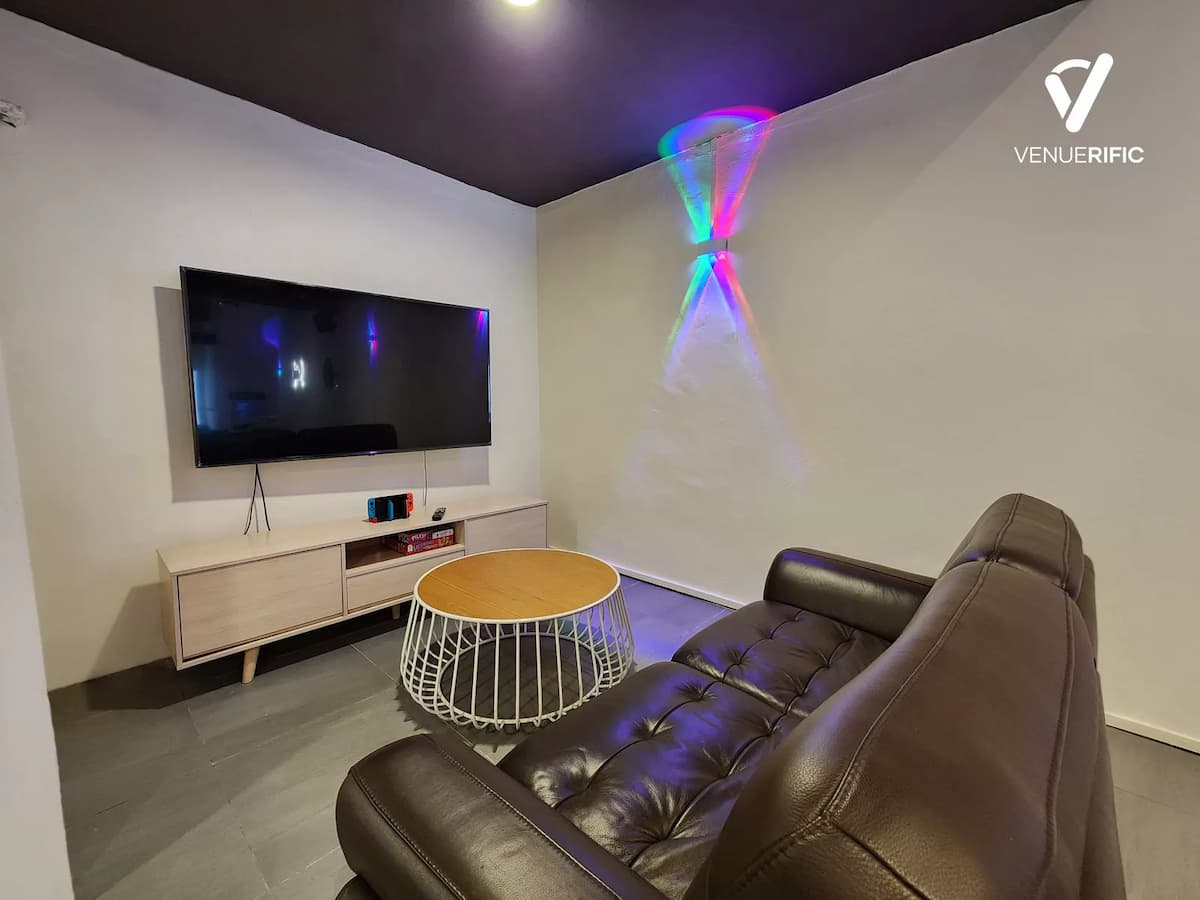 Modern lounge room with leather sofa, round coffee table, wall-mounted TV, and colorful light projection on a white wall.