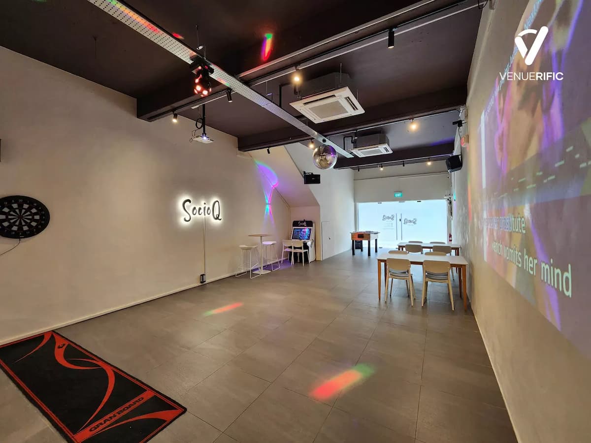 SocioQ event space with open-plan layout, projector screen, minimalist white walls, casual seating and tables, ambient disco ball lighting, and flexible setup for workshops or presentations.