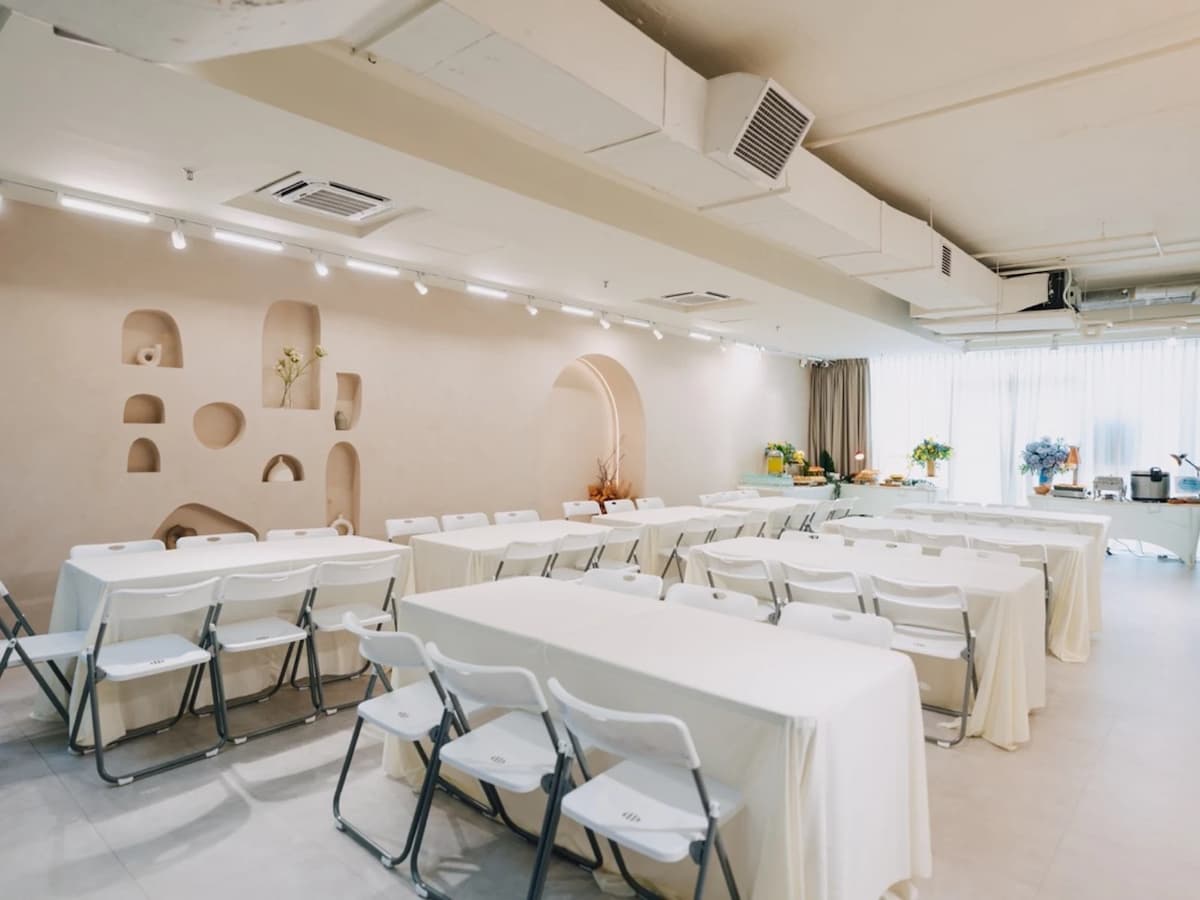 A bright, modern workshop space with long tables draped in white linens, rows of white folding chairs, and a textured feature wall with arched niches