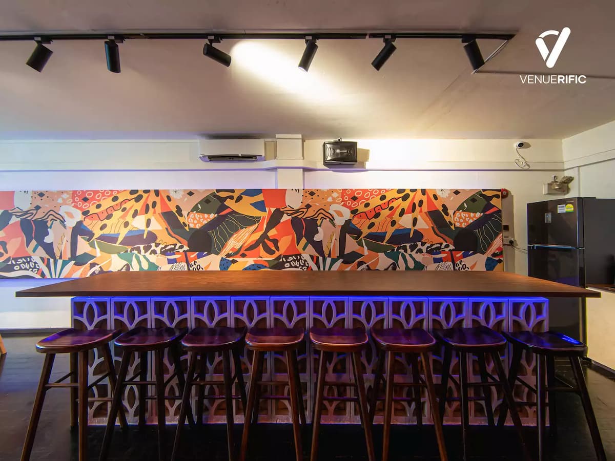 Close-up of a wooden bar counter with blue LED lattice base and a row of bar stools, set against a wide vibrant abstract mural wall