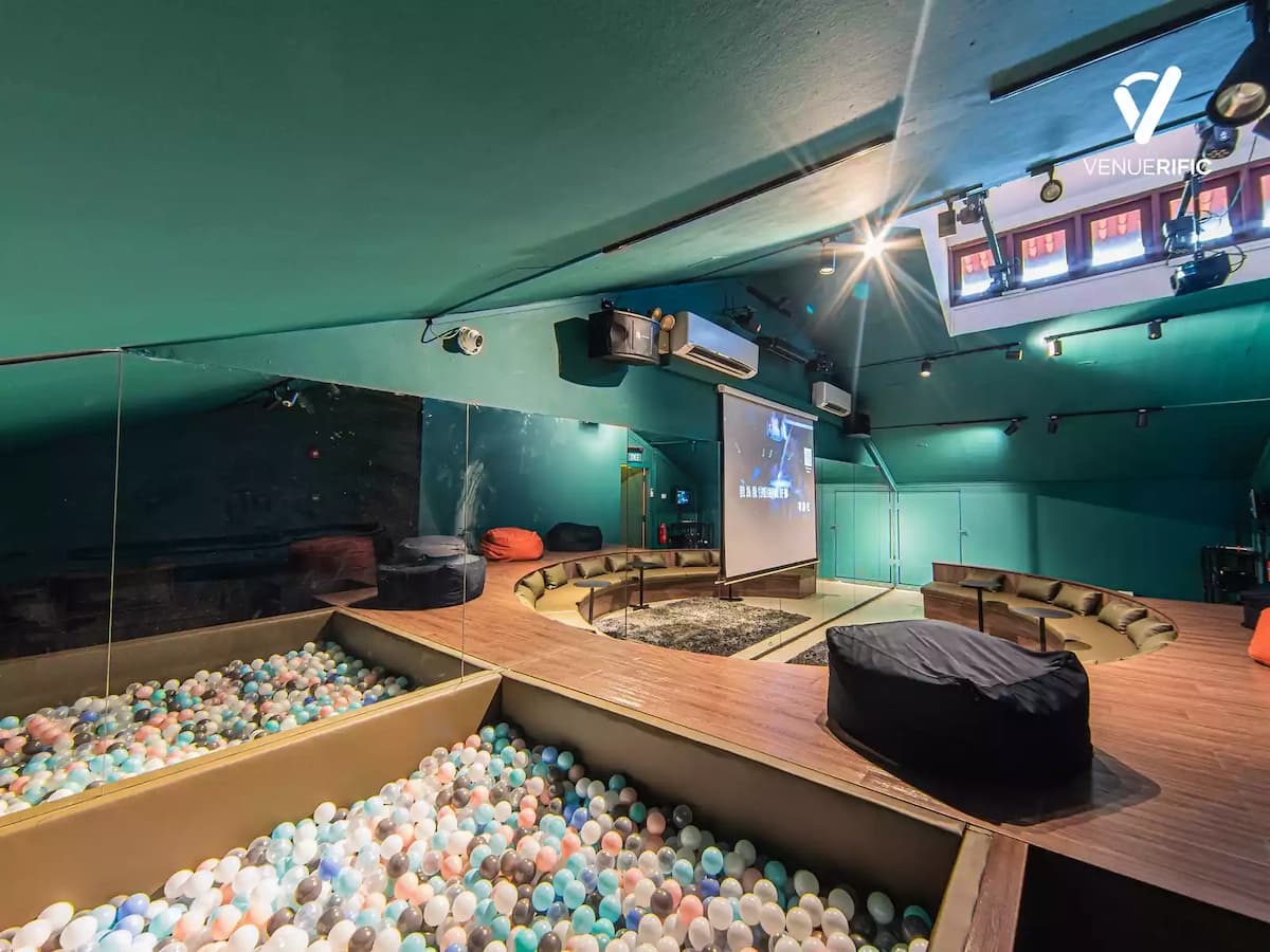Indoor entertainment room with a large colourful ball pit in the foreground, circular sunken lounge seating, projection screen, and teal-painted walls