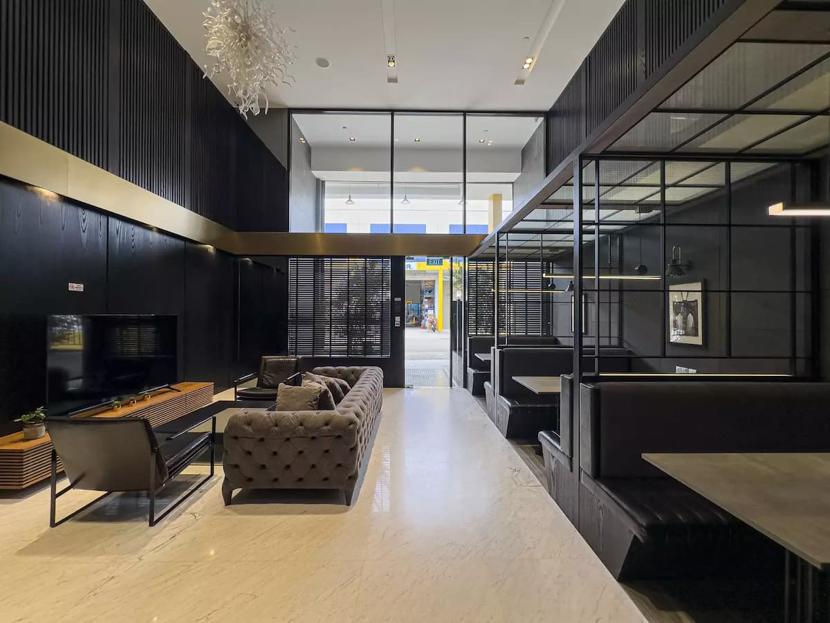 A modern lounge area featuring a tufted grey sofa, a sleek black media wall, and private booth seating under a high ceiling.