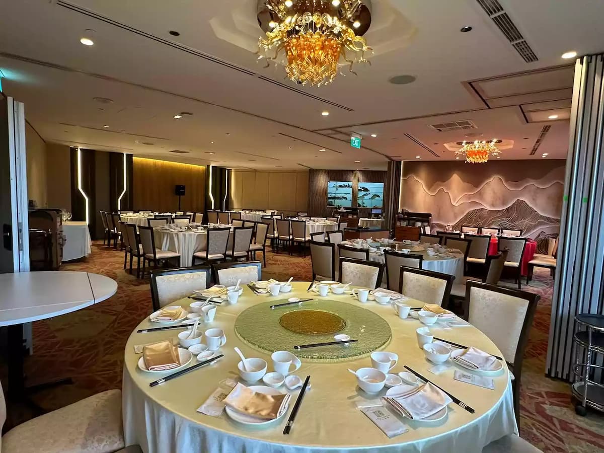 Spacious banquet hall with round tables, elegant table settings, warm lighting, and statement chandeliers.