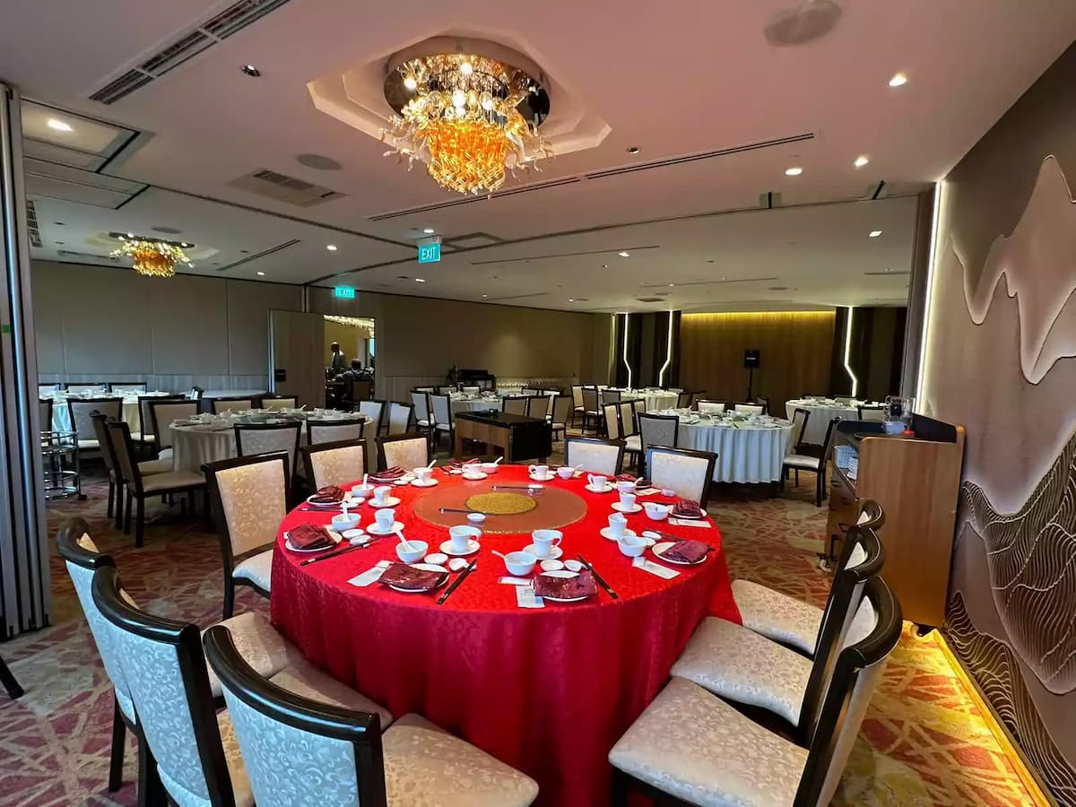 Elegant banquet room with round dining tables, red table setting, crystal chandeliers, and warm ambient lighting.