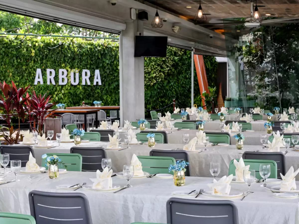 Elegant restaurant event setup with long banquet tables, folded napkins, and greenery at ARBORA.