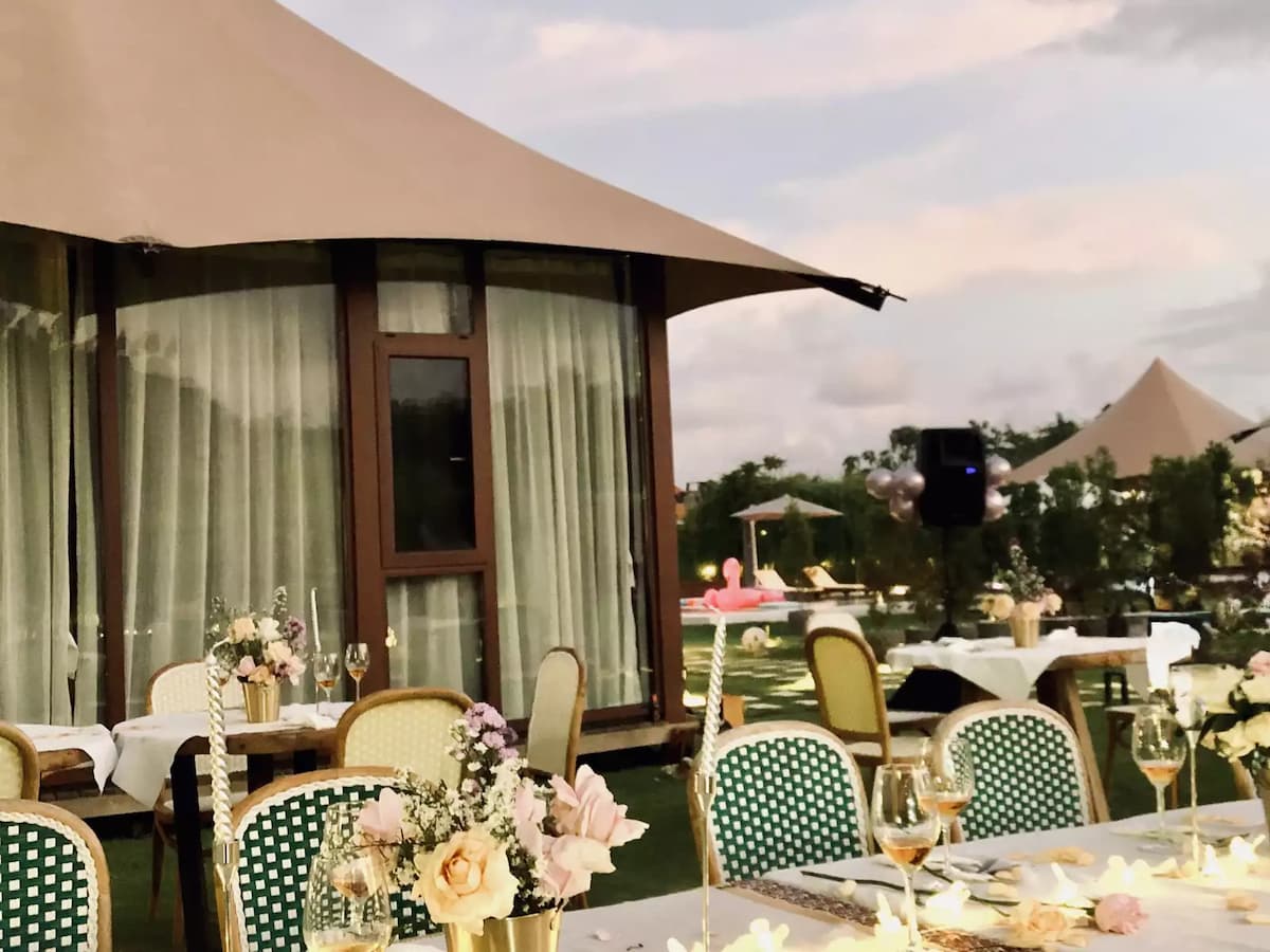 Outdoor garden dining setup beside modern tented villas with decorated tables and pool view at dusk.