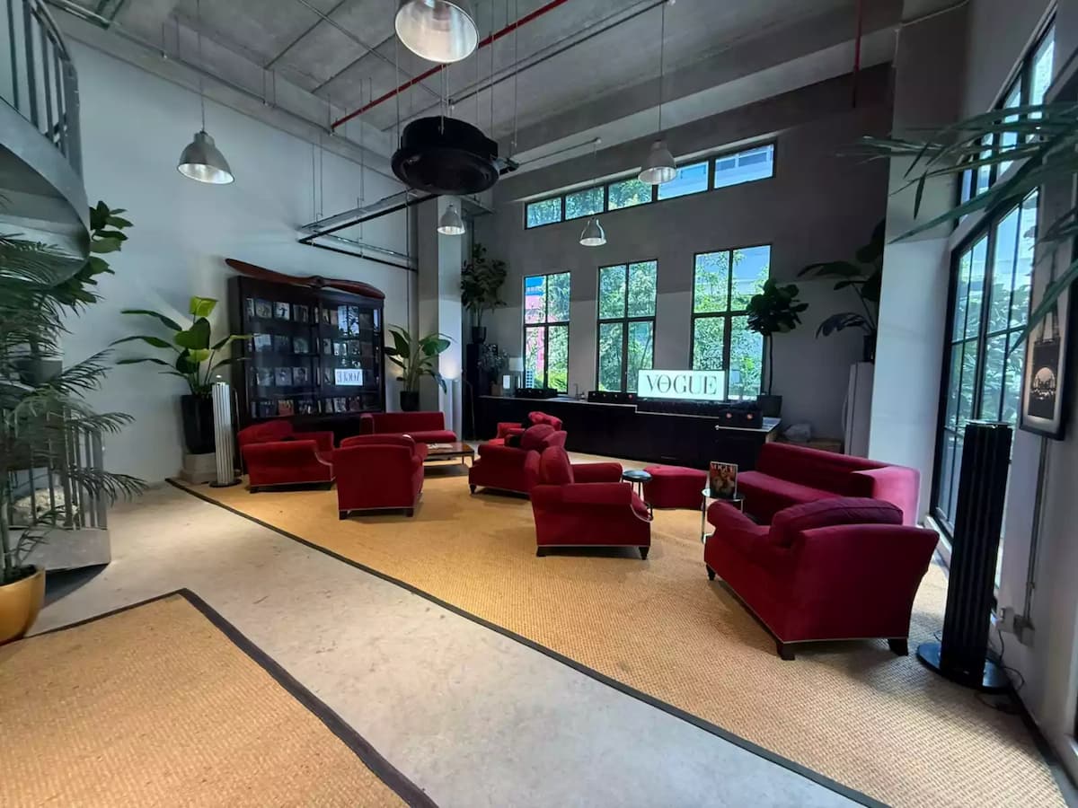 Loft-style lounge with red sofas, high ceilings, and large windows.