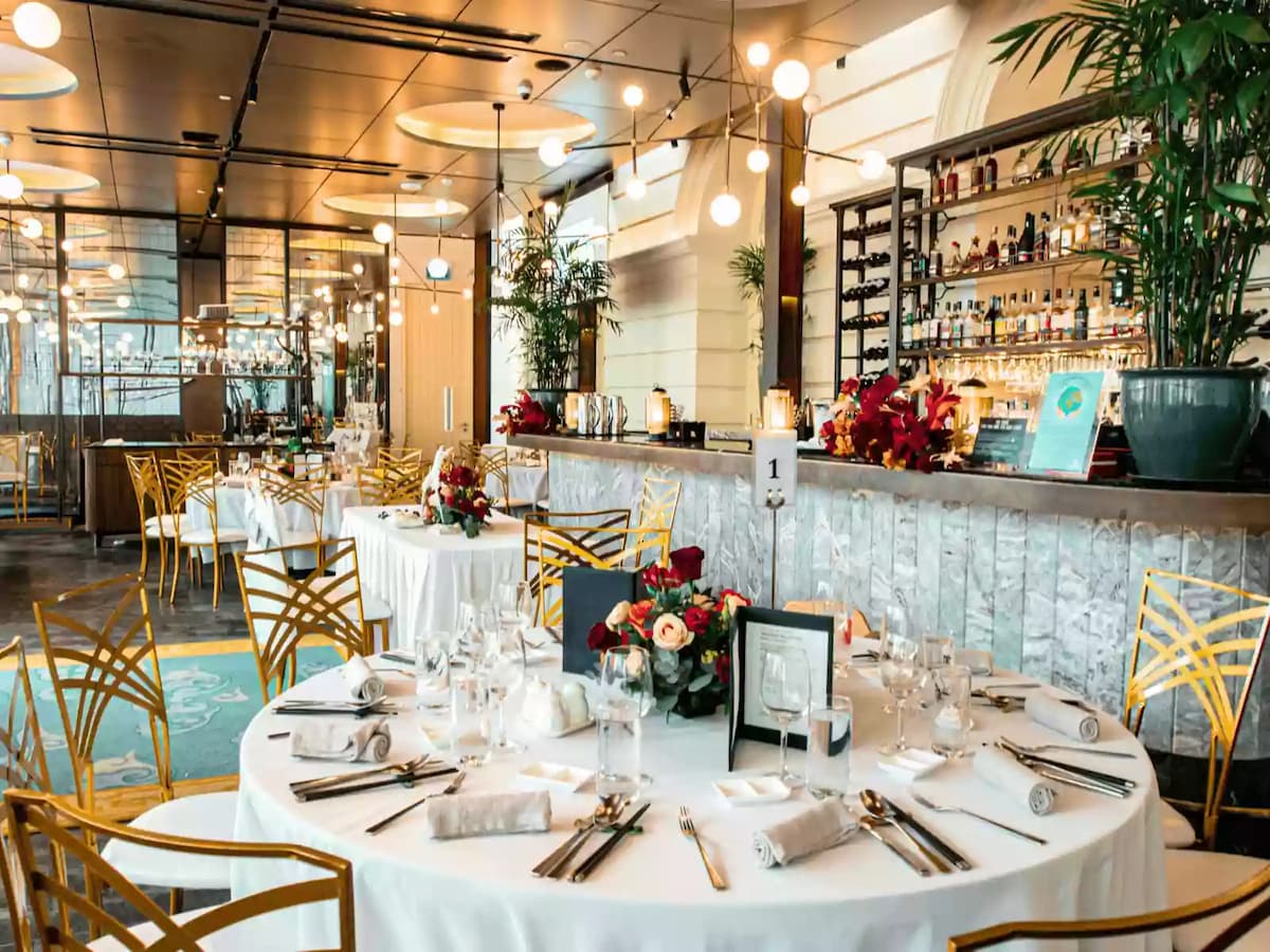 Elegant restaurant event setup with round tables, floral centerpieces, and bar.