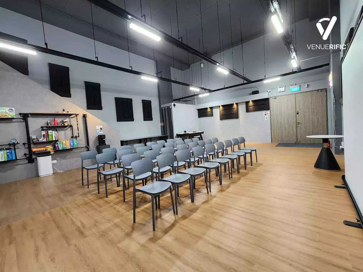 Modern classroom-style event room with rows of chairs, wood flooring, and an open industrial ceiling.