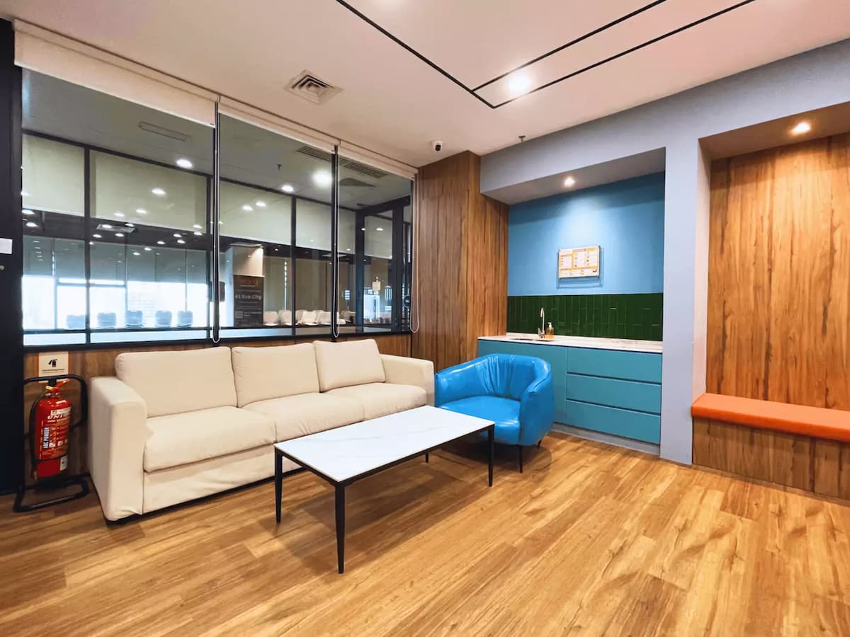 cream sofa and blue armchair around a marble coffee table beside a pantry counter in a networking breakout lounge in kuala lumpur