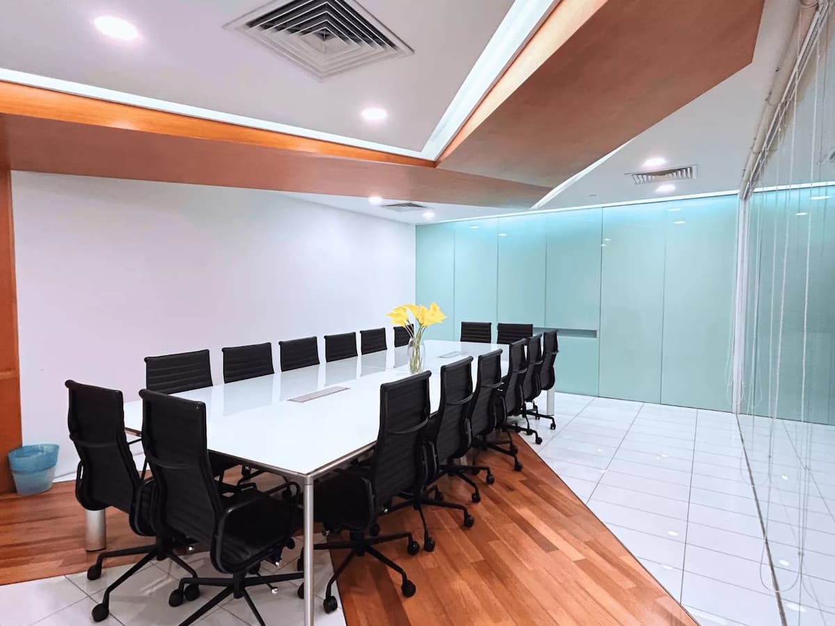 Modern boardroom with long white conference table, black swivel chairs, and glass partition walls.
