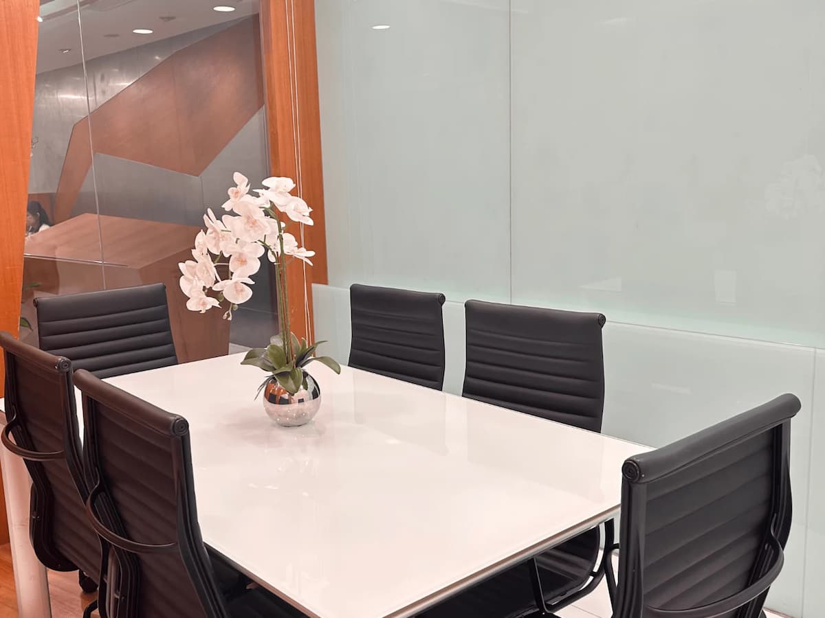 Compact meeting room with white table, black chairs, wood panel walls, and frosted glass partition.