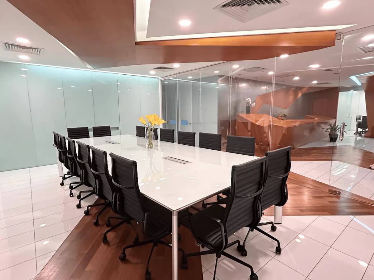 Modern boardroom with long white conference table, black swivel chairs, and glass partition walls.