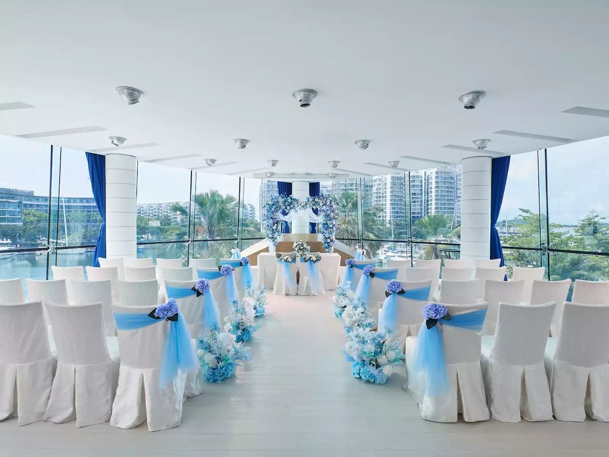 Waterfront wedding ceremony with white chairs, blue floral aisle, and marina views.