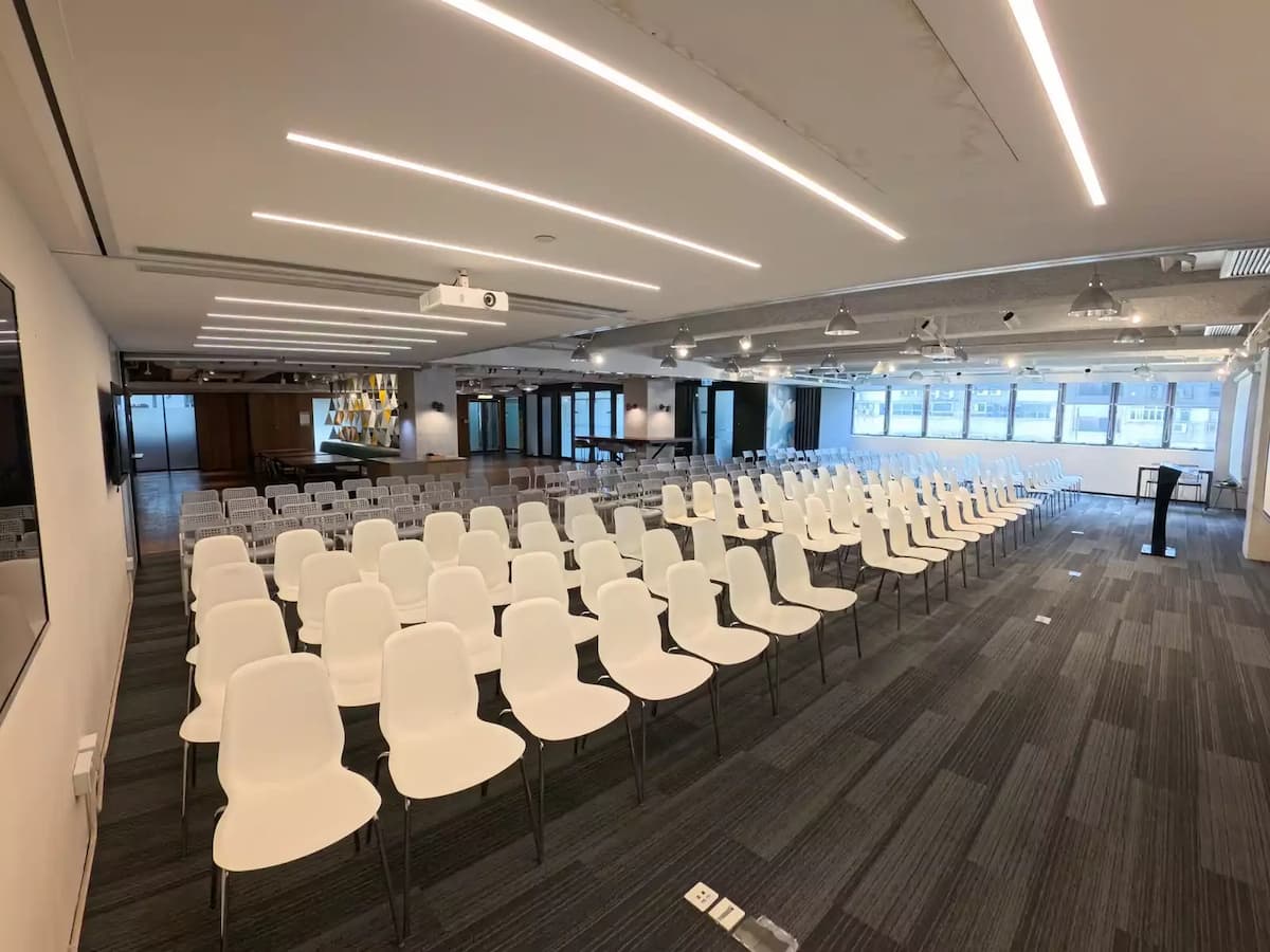 Conference-style event space with rows of white chairs, projector setup, and modern industrial ceiling lighting.