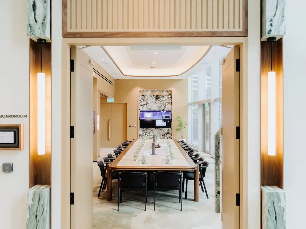 View into a modern boardroom with long conference table, black chairs, and built-in screen display.