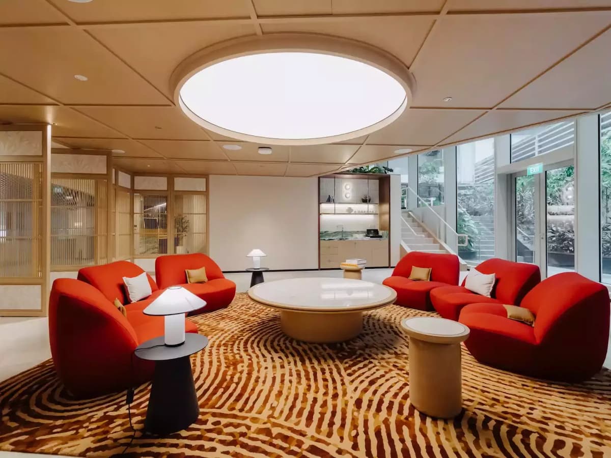 Contemporary lounge with red curved sofas, round coffee table, patterned rug, and large circular ceiling light.