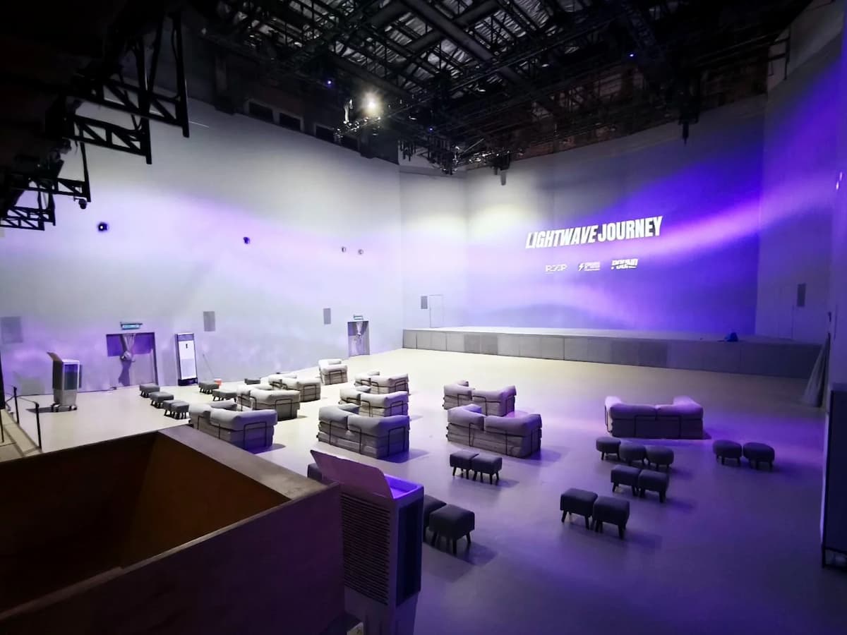 Large event hall with lounge seating, stage platform, and purple lighting projection on high white walls.
