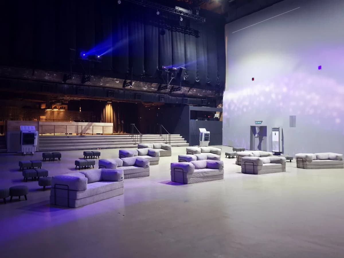 Spacious event hall with modular lounge seating, stage area, and soft ambient lighting for a relaxed setup.