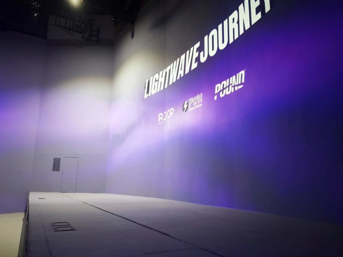 Minimalist stage setup with a wide platform, high white walls, and purple light projection branding.