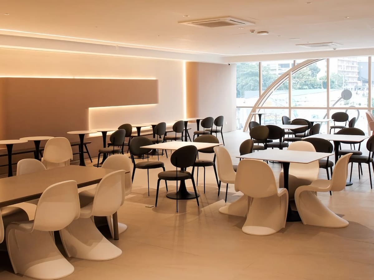Bright modern café-style event space with sculptural chairs, minimalist tables, and large windows.