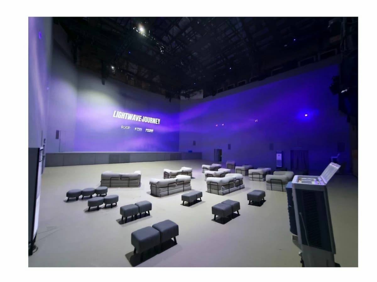Large event hall with modular lounge seating, open floor layout, and purple lighting projected on high white walls.