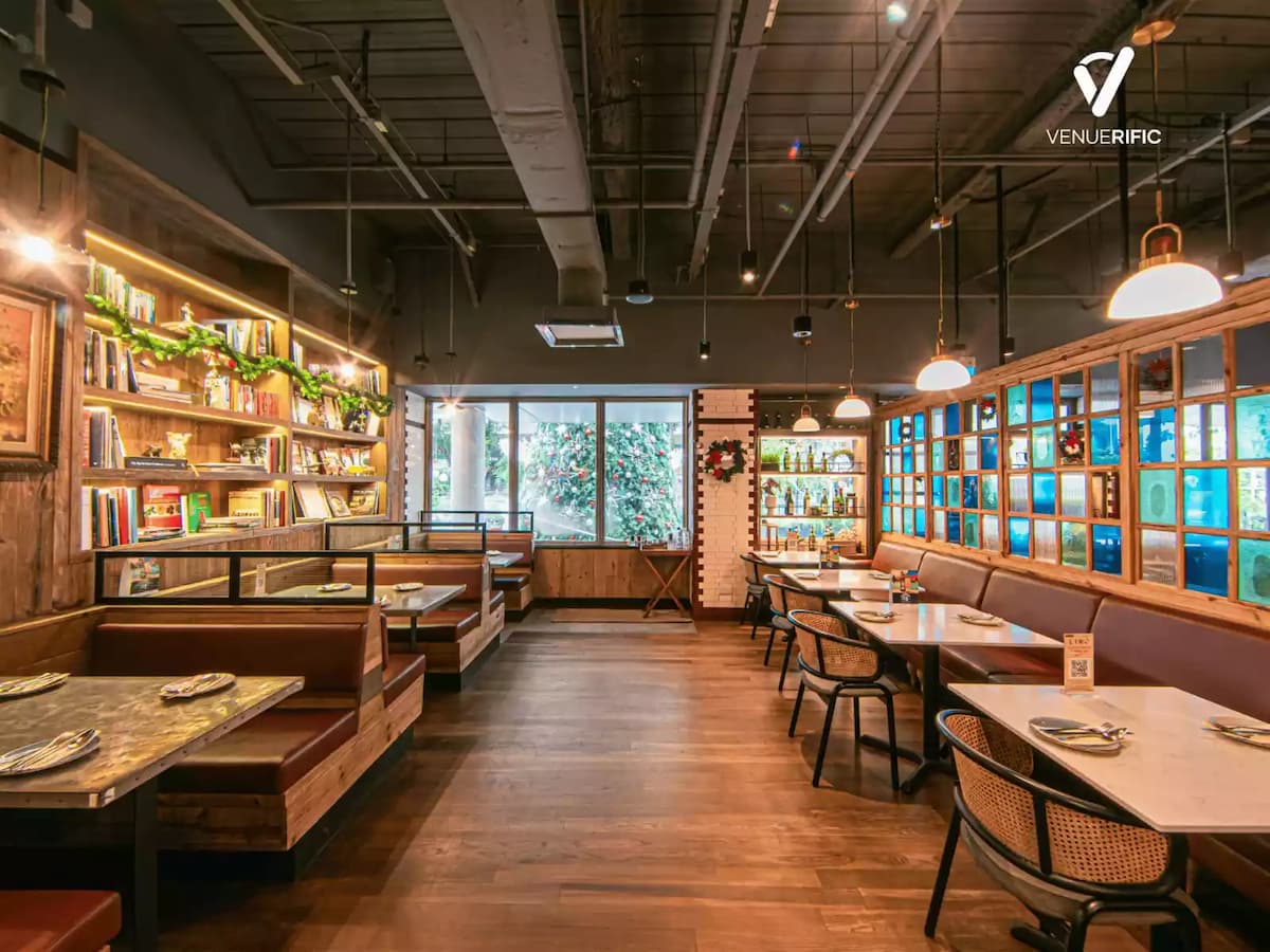 Warm, rustic restaurant interior with wooden booths, cozy table seating, hanging lights, and glass-panelled walls.