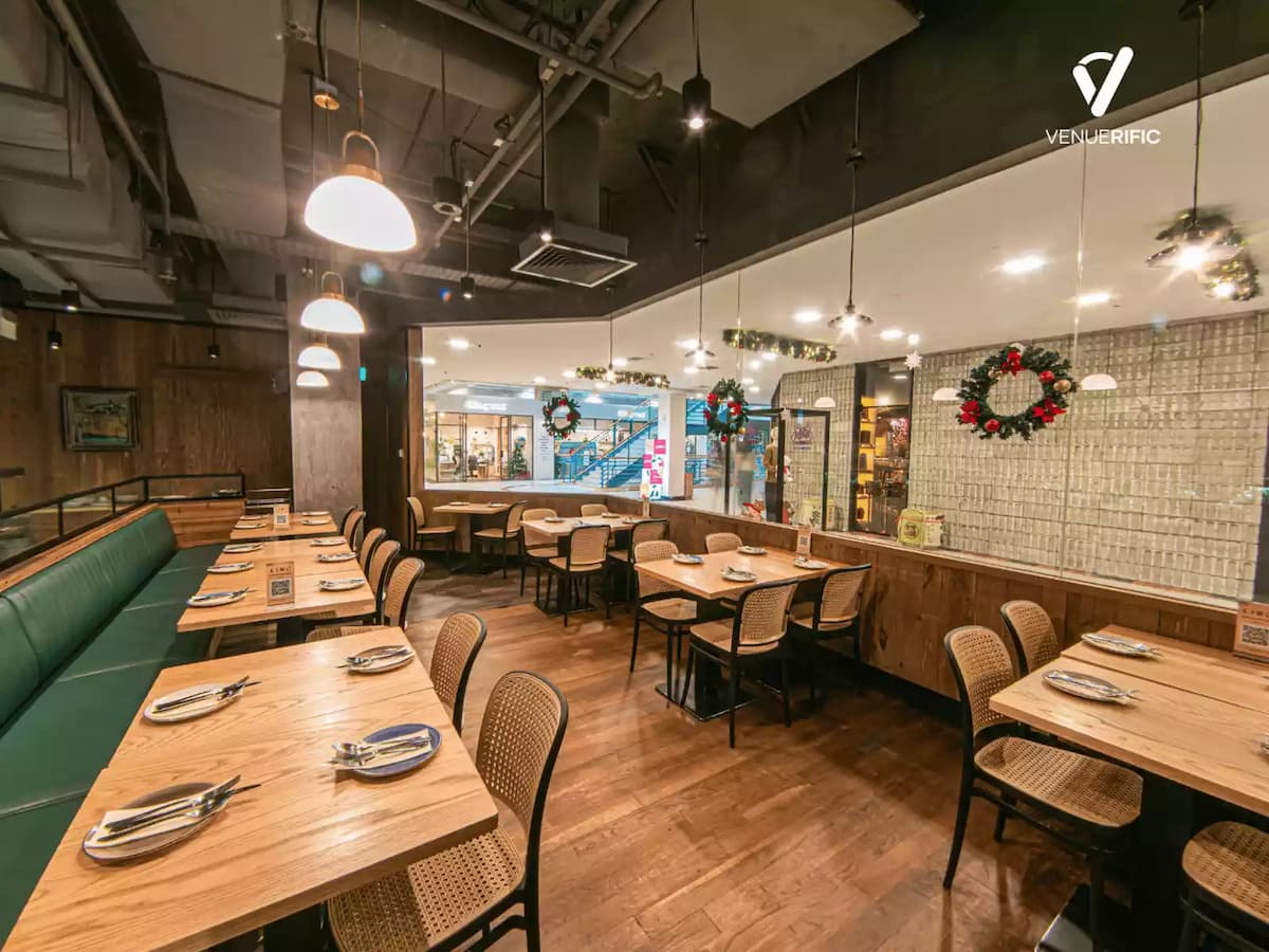 Warm, modern restaurant dining area with wooden tables, green banquette seating, pendant lights, and festive wreath decor.