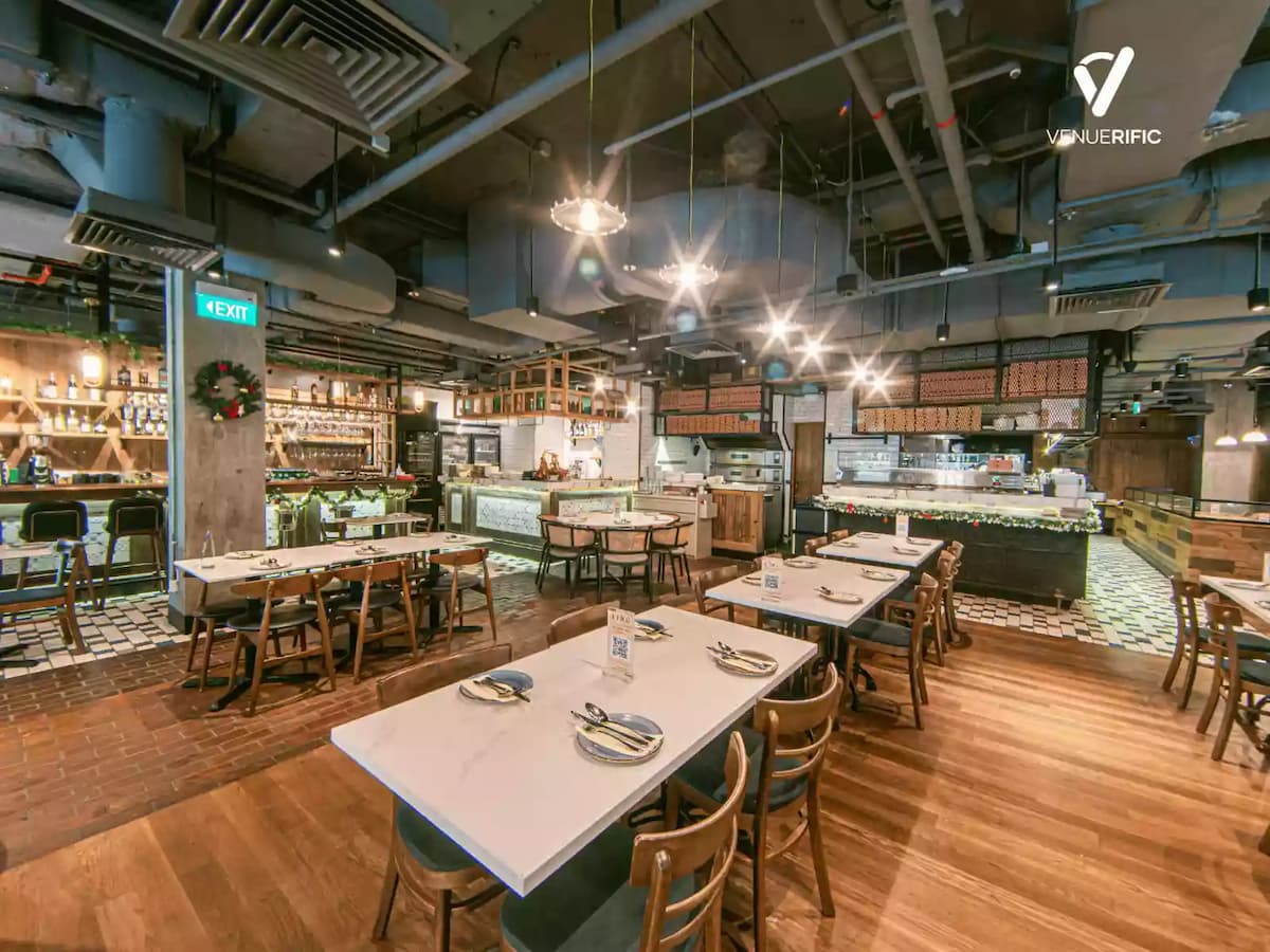 Spacious modern restaurant interior with marble-top tables, wooden chairs, open kitchen counters, warm lighting, and industrial ceiling design