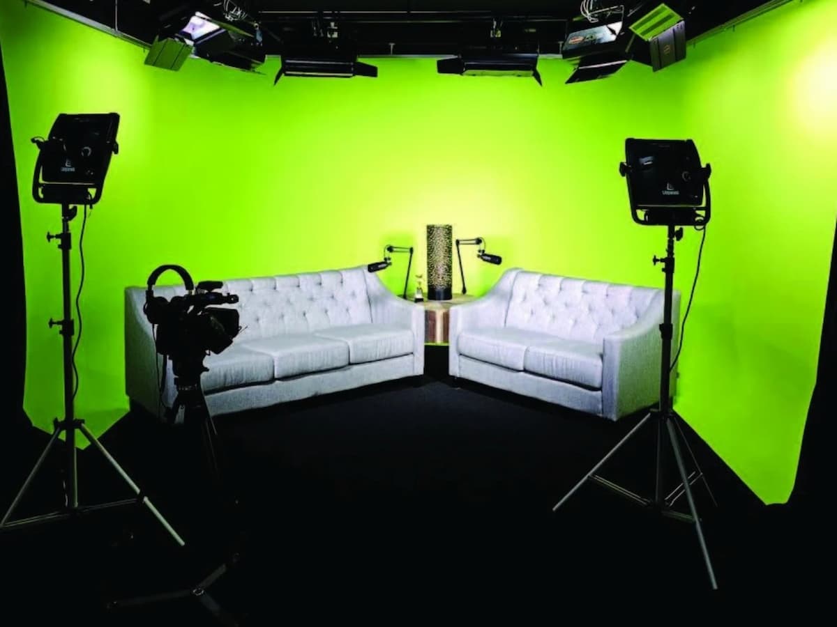 white tufted sofas and studio lights facing a green screen wall in a talk show filming studio in kuala lumpur