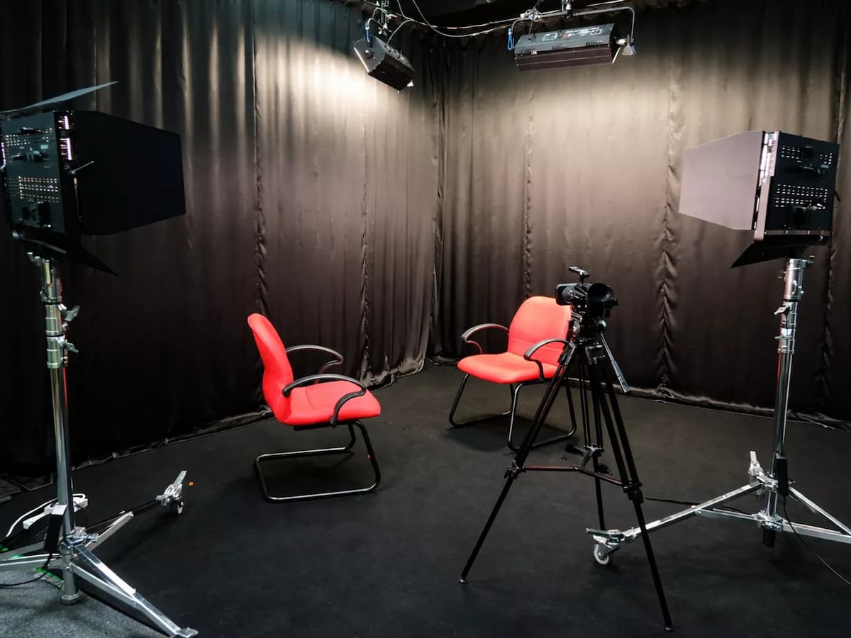 two red chairs and a camera on a tripod set up for an interview in a black curtain video recording studio in kuala lumpur