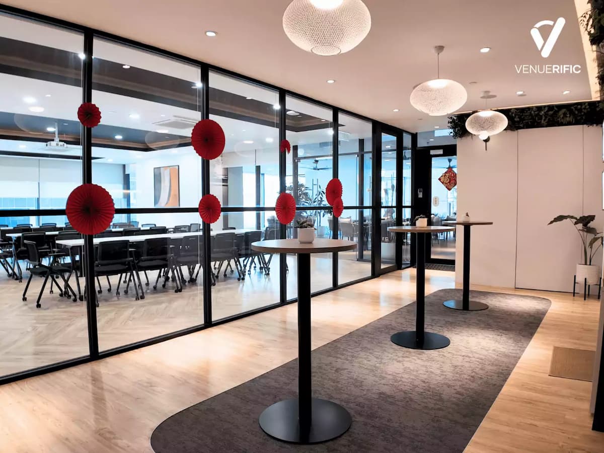 Networking area with high tables and glass-walled meeting rooms decorated with red paper accents.