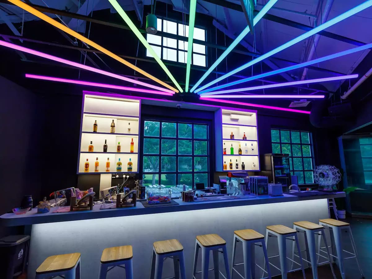 Modern bar with illuminated back shelves, neon ceiling light strips, and high stools.