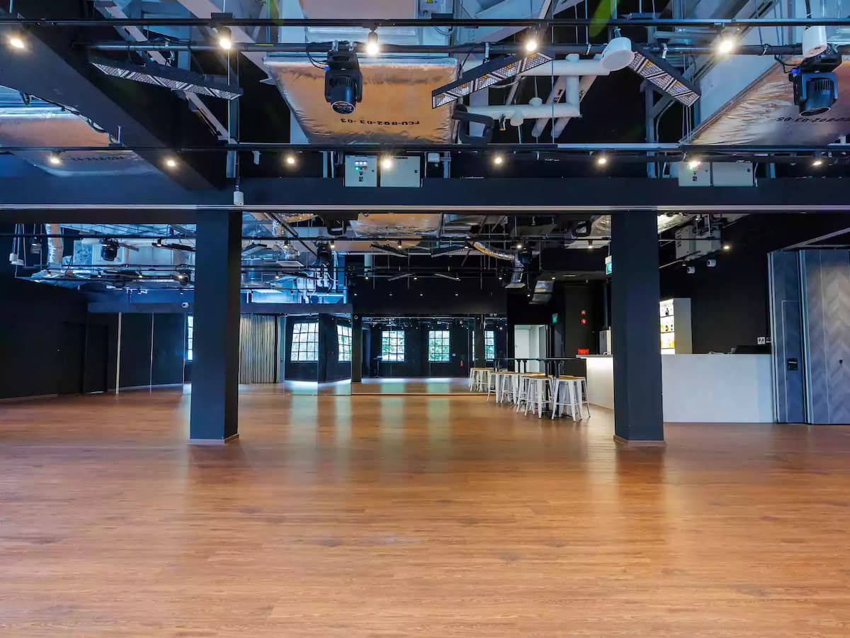 Open-plan event space with wooden floors, mirrored wall, exposed ceiling, and modern lighting.