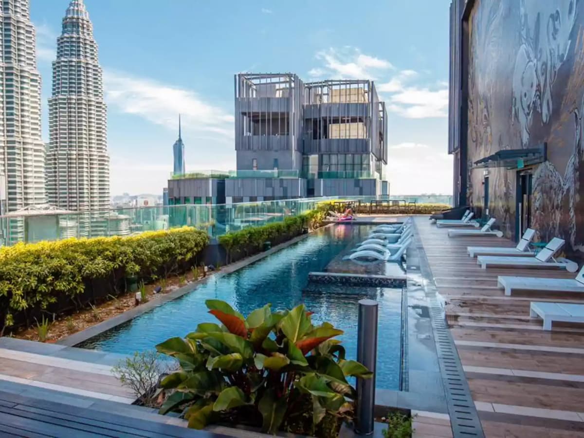 Rooftop infinity pool with lounge chairs and skyline views, including the Petronas Twin Towers in the background.