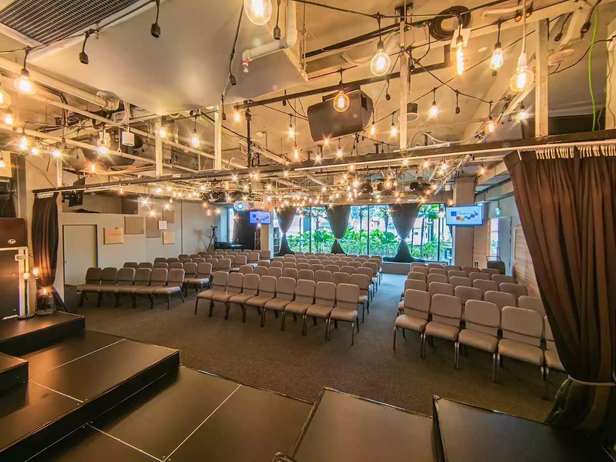 Modern event space with theatre-style seating, warm string lighting, and presentation screens—ideal for conferences, seminars, workshops, talks, and corporate training sessions.